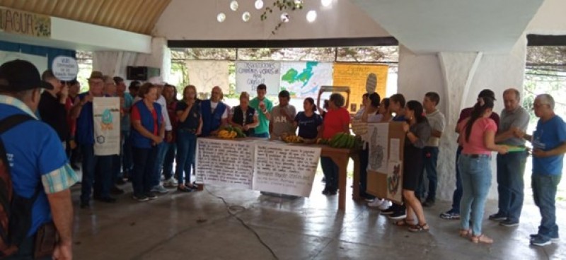 A large group of people stood around a table holding and displaying banners, posters, and regional produce